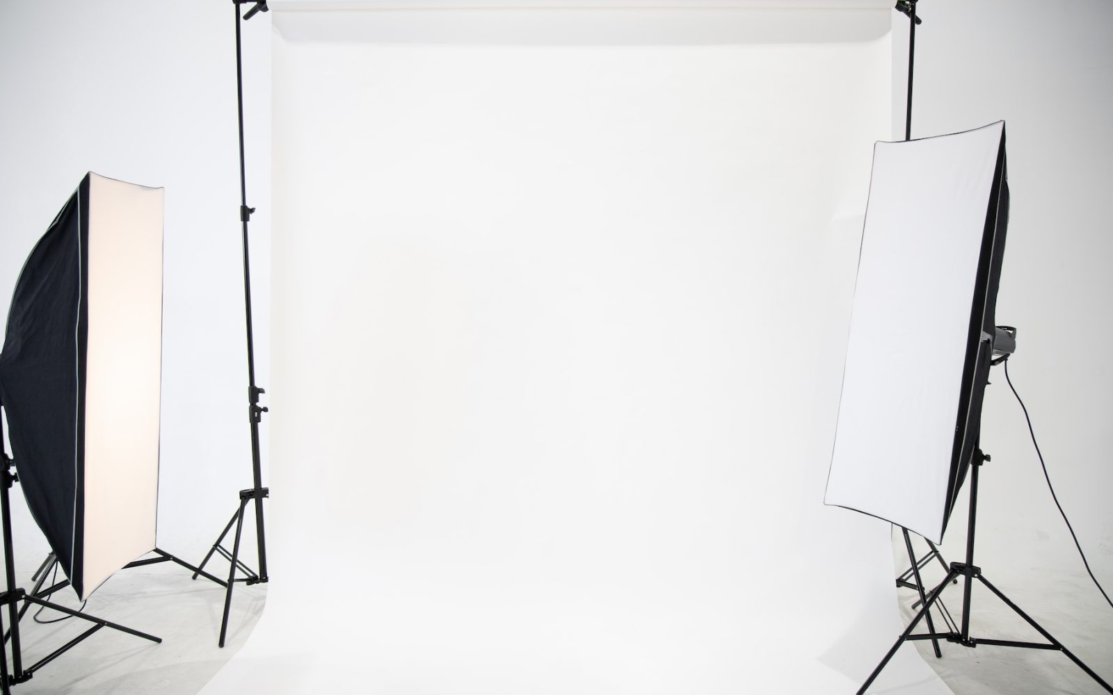 Studio is empty of the photographer with professional lighting arrangements. Flash, light equipment and white background scenes prepared for shooting in the studio. Modern photographer studio.